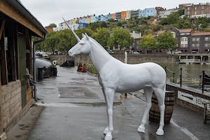 A large white unicorn stands in front of painted houses in Bristol