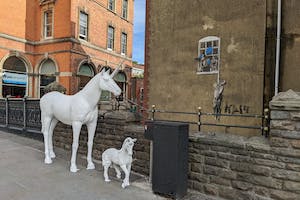 A large and small unicorn stand infront of a piece of art from the artist Banksy